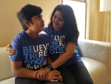 A mother sitting on a couch near a window with her arms around her autistic son