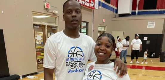 Two siblings stand on a basketball court in matching shirts 