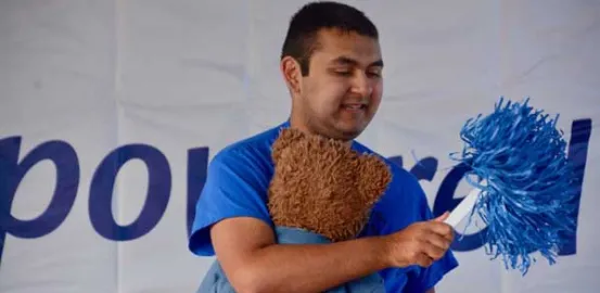 Andrew at an Autism Speaks Walk holding a stuffed bear and blue pom-pom