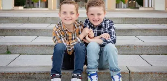 Twin toddlers sitting on concrete steps while linking arms