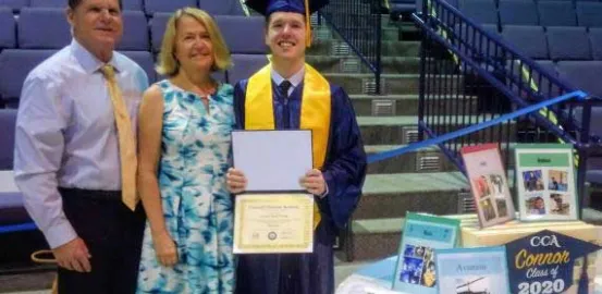 Connor at graduation holding his degree next to his mom and dad