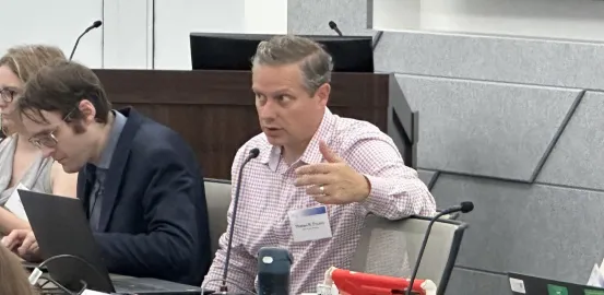 Tom Frazier sitting at conference table, speaking into microphone