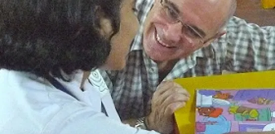 Jonathan Green kneeling down next to a table to talk to a young girl