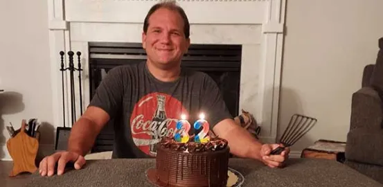 Josh smiling in front of a birthday cake on his 32nd birthday