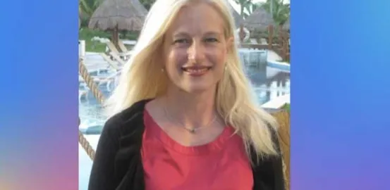 women in a pink t-shirt and black top smiles at the camera in front of palm trees and a pool