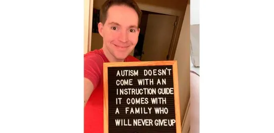 Man in a red shirt holds a letterboard sign that reads "Autism doesn't come with an instruction guide, it comes with a family who will never give up" 