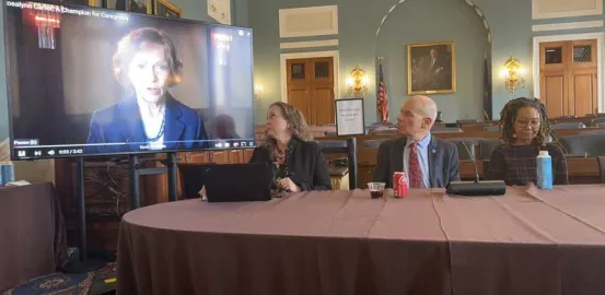 Three panelists watching TV for video of Former First Lady Rosalynn Carter speaking about caregivers