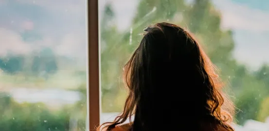 Woman looking at a lake and mountains out a window 