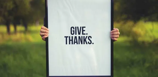 Woman holding a sign that says 'Give Thanks'