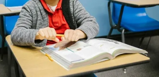 a frustrated child sitting at a desk trying to snap a pencil in half