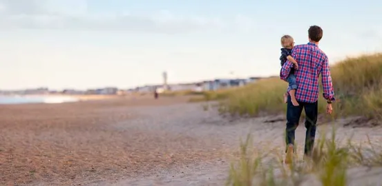 a man in a plaid shirt walking on the beach and carrying a child