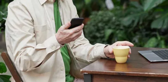 an older man sitting outside with a coffee and looking at his cell phone