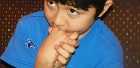 autistic child in a blue shirt putting his hands near his mouth and avoiding eye contact