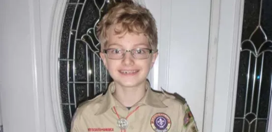 young boy with blonde hair and glasses wearing a Boy Scout uniform