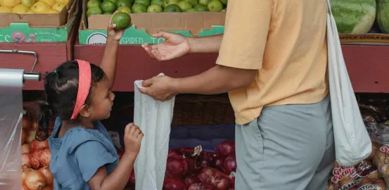 child helping mother put produce in a bag at grocery store