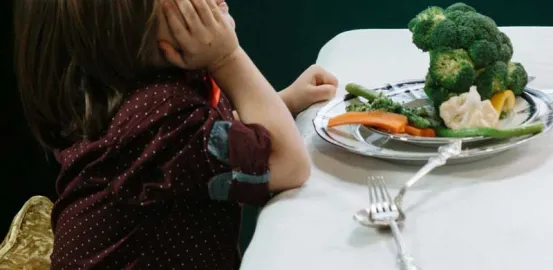 child looking away from a plate of vegetables on the table