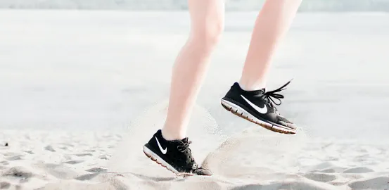 close up of someone exercising on sand beach wearing black sneakers