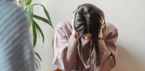 girl in a pink hoodie with her head down and hands covering her ears