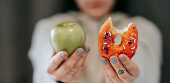 girl with nails painted blue holding up a donut in one hand and an apple in the other