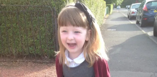 little girl wearing a red cardigan with a bow in her hair