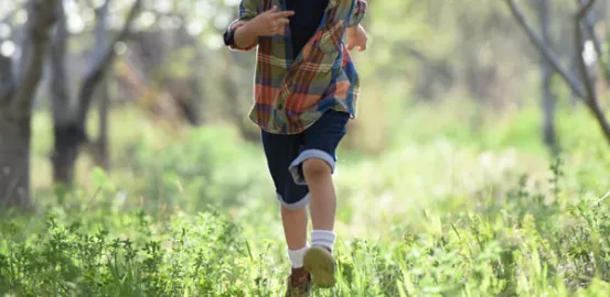 little boy in a plaid shirt running through the forest