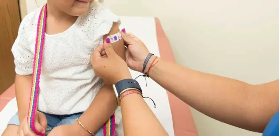 little girl looking down and smiling as a doctor puts a bandage on her arm