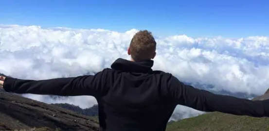 man on a mountain top looking at the clouds