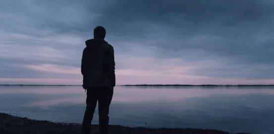 man's silhouette standing in front of a lake at sunset