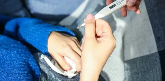 mother handing a thermometer to a child in a blue sweater