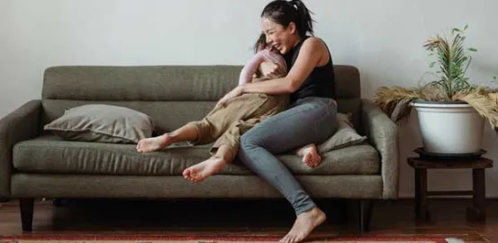 mother laughing and playing with her child on the couch