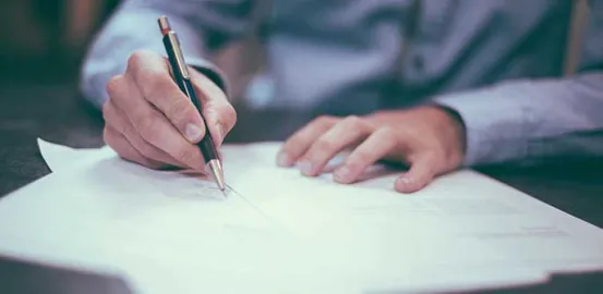 person in a blue button up shirt writing with a pen