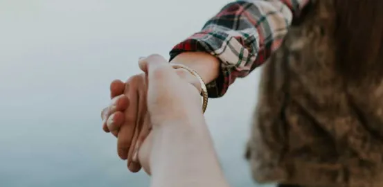 person in a flannel shirt and fur vest holding the hand of someone behind them