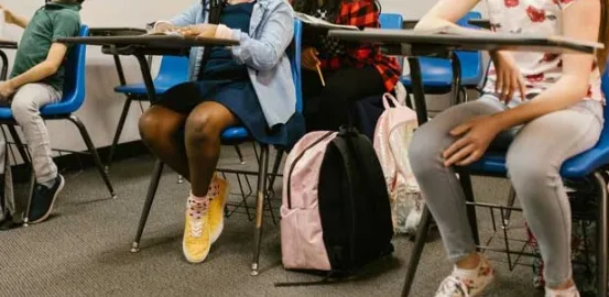 school students sitting in desks with their backpacks at their feet