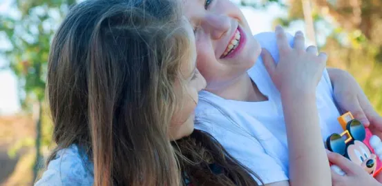 siblings hugging and laughing while playing outside with a Mickey Mouse toy