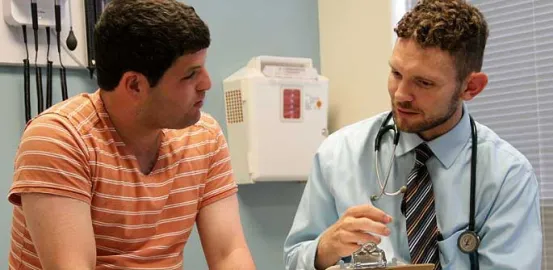 teen in an orange shirt talking to his doctor