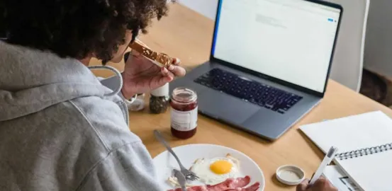 teen sitting at kitchen table eating a working on laptop