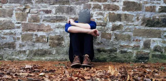 teen sitting on the ground covering their face