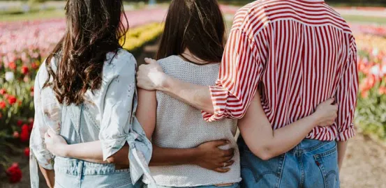 three girls looking at a field of flowers with their arms around each other