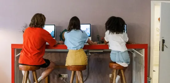 three teens sitting at a table on laptops