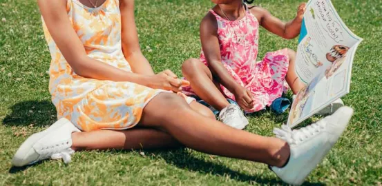 two Black children sitting in the grass and looking at a book