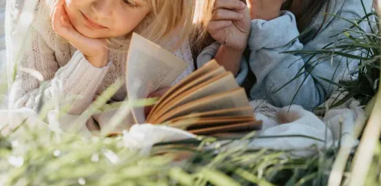 two little girls laying in the grass reading books