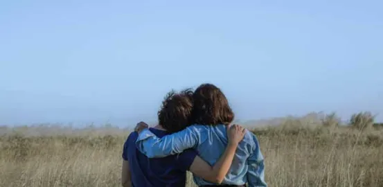 two women with their arms around each other in a field