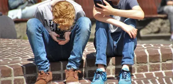 two young boys sitting outside looking at their cell phones