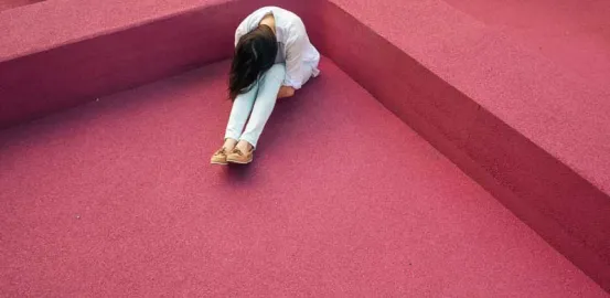 woman in a red room with her head down resting on her knees