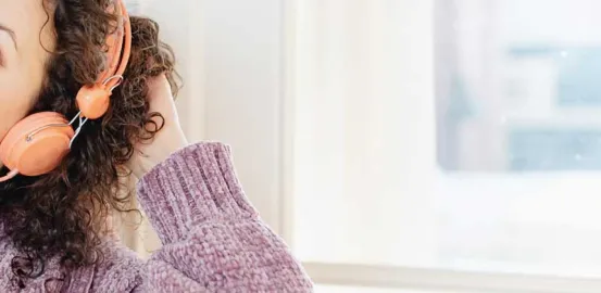 woman touching her curly brown hair and wearing orange headphones