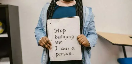 young girl holding a sign that says 'stop bullying me. I am a person'