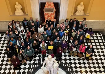 Photo taken from a second floor landing, of a large group of advocates standing on a black and white checkered floor in the capitol atrium