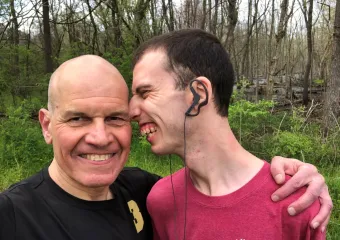 Stuart Spielman looking at camera smiling with arm around his son's shoulder. Zak smiles while leaning his face towards side of Stuart's head.