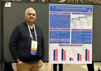 Vijay Vasudevan standing in front of a poster with his research