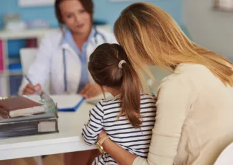 A mother and young daughter sitting at a desk across from a female doctor.